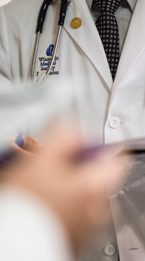 An embroidered W crest is pictured on a medical student’s white coat during floor rounds.