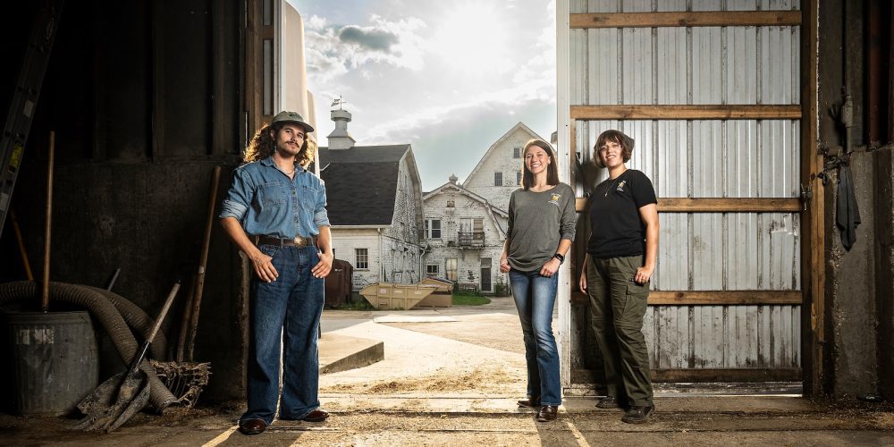 Three undergraduate students stand just inside the door of a dairy barn on the campus of UW–Madison