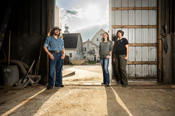 Three undergraduate students stand just inside the door of a dairy barn on the campus of UW–Madison