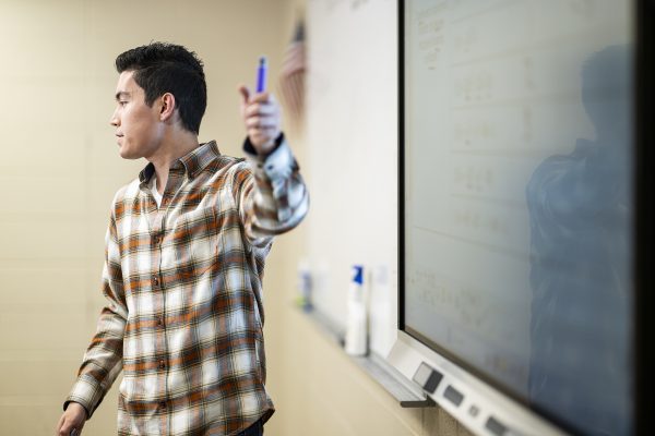 Reed Trueblood gestures with a dry erase marker in front of a whiteboard in his math classroom.