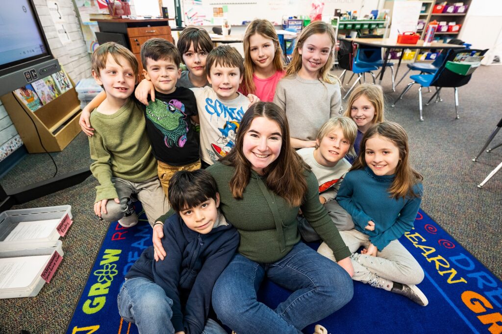 Group of smiling children with a teacher in a colorful classroom setting.