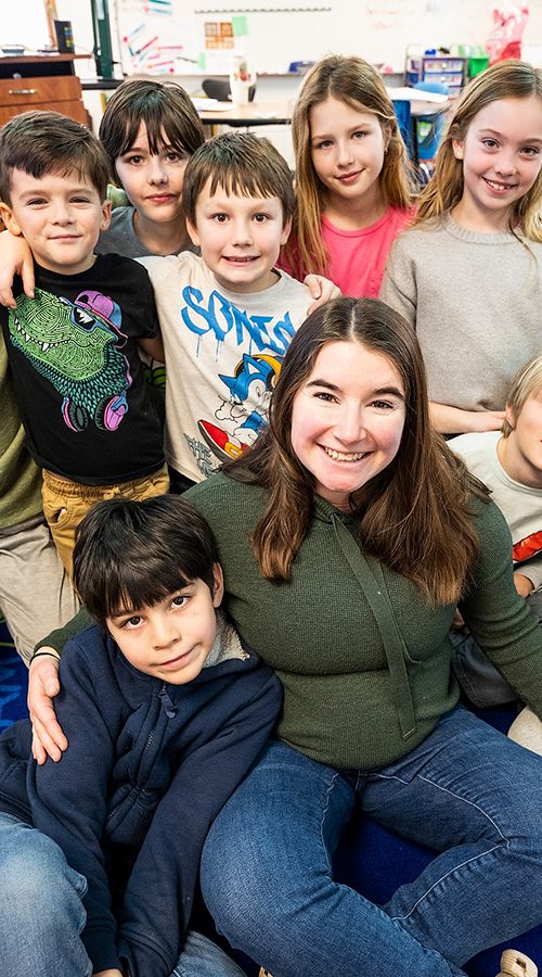 Group of smiling children with a teacher in a colorful classroom setting.