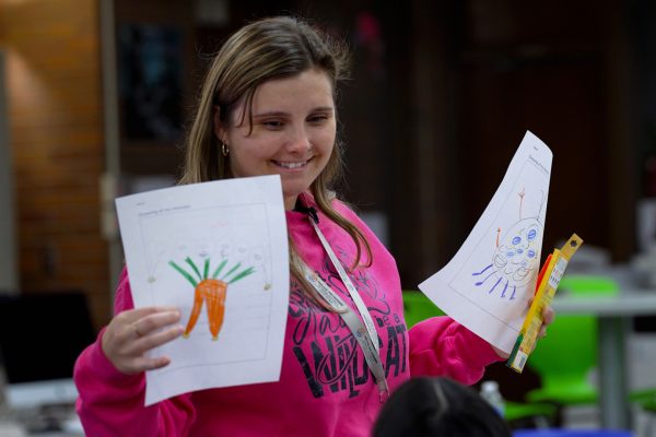 Ania Kotecki smiles while holding up a piece of paper that a student has drawn on.