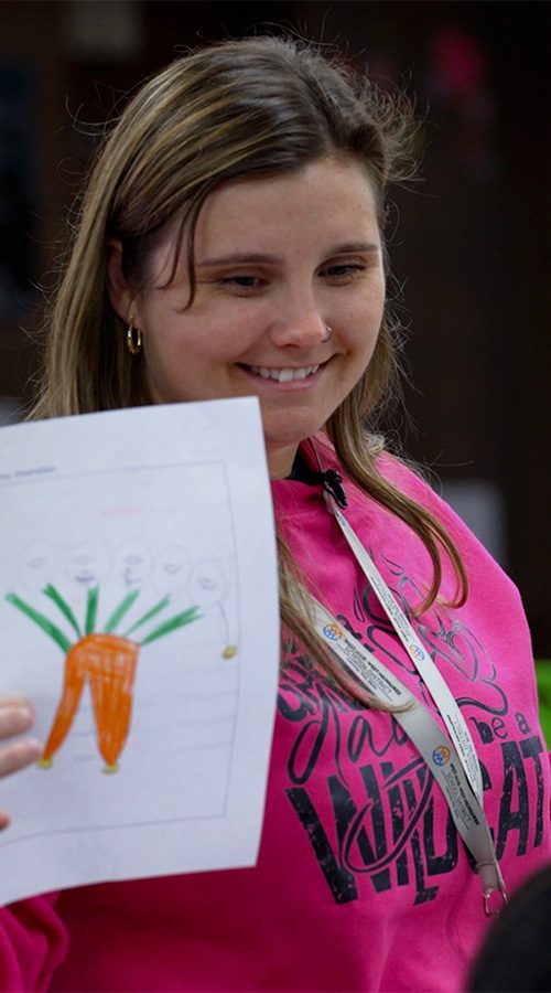 Ania Kotecki smiles while holding up a piece of paper that a student has drawn on.