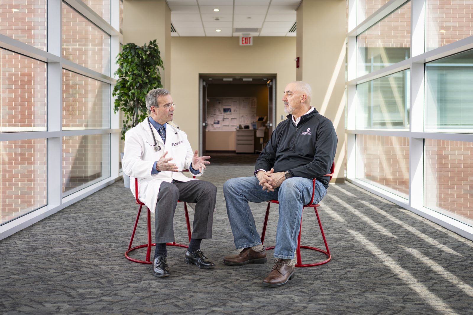 Michael Medich and Joseph Holt have a conversation sitting in two red Terrace chairs in the middle of a skybridge at the Aurora Baycare Medical Center in Green Bay.