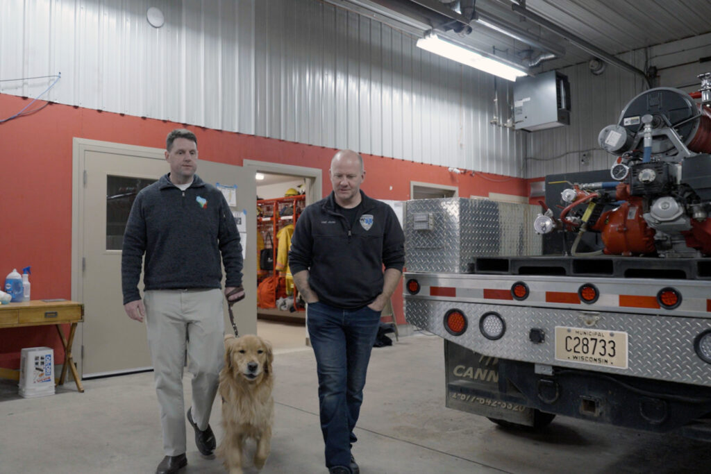 Small and Joling walk with a golden retriever past a fire truck at a station