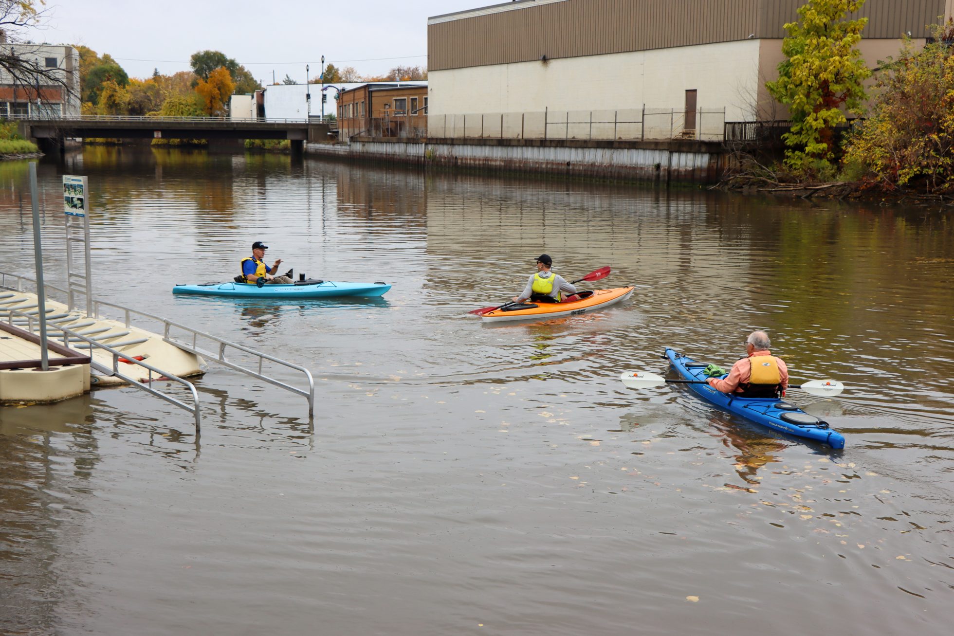 Three people are in colorful kayaks in the river.